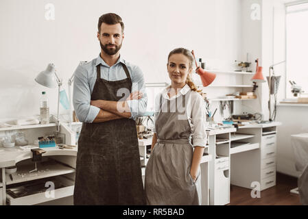 Geschäft für ein Paar. Portrait von lächelnden Paar in Schürzen an ihren Schmuck Workshop stehen und von der Kamera. Schmuck. Geschäft Stockfoto