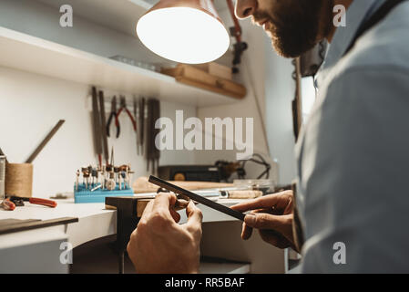 Auf einen Prozess konzentriert. Nahaufnahme eines jungen männlichen Juwelier arbeiten und die Gestaltung eines unfertigen Ring mit einem Werkzeug in der Werkstatt. Schmuck. Busines Stockfoto