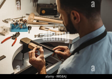 Zarte Schmuck arbeiten. Nahaufnahme eines männlichen Juwelier arbeiten und die Gestaltung eines unfertigen Ring mit einem Werkzeug in der Werkstatt. Schmuck. Business. Je Stockfoto