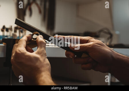 Ein Meisterwerk. Nahaufnahme der Hände eines männlichen Juwelier arbeiten und die Gestaltung eines unfertigen Ring mit einem Werkzeug auf der Workbench in der Werkstatt Stockfoto