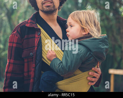 Ein junger Vater mit einem Kleinkind in einer Schlinge ist den Wald erkunden Stockfoto