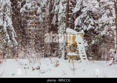 Einfache Holz- Jagd im Schnee bedeckt. Jagd Hirsch blind neben einer Reihe von Bäumen im Winter Landschaft Stockfoto