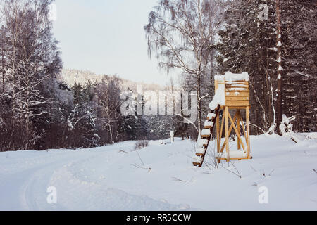 Einfache Holz- Jagd im Schnee bedeckt. Jagd Hirsch blind neben einer Reihe von Bäumen im Winter Landschaft Stockfoto