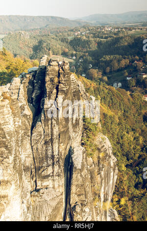 Felsformation in der Sächsischen Schweiz. Felsen aus dem Elbsandsteingebirge Turm mit Dorf und Bäume im Herbst Stimmung sind im Hintergrund Stockfoto