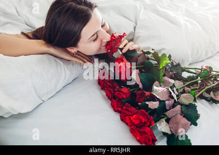 Junge Frau gefunden Blumenstrauß aus Rosen im Bett. Happy girl duftende Blumen. Tag der Frauen überraschen Stockfoto