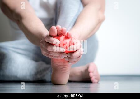 Causian Mann hält Hände an seine schmerzende Füße, Schmerzen im Fuß, die rote Farbe wird der Schmerz Stockfoto