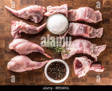 Oben auf Ansicht Portioniert Kaninchen Beine und Sattel mit Kräutern und Gewürzen auf butcher Board. Stockfoto
