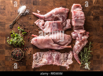 Oben auf Ansicht Portioniert Kaninchen Beine und Sattel mit Kräutern und Gewürzen auf butcher Board. Stockfoto