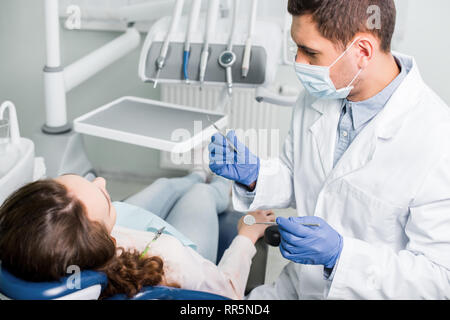 Schwere Zahnarzt in Latex Handschuhe und Maske Holding zahnmedizinischen Ausrüstung in der Nähe der Patientin Stockfoto