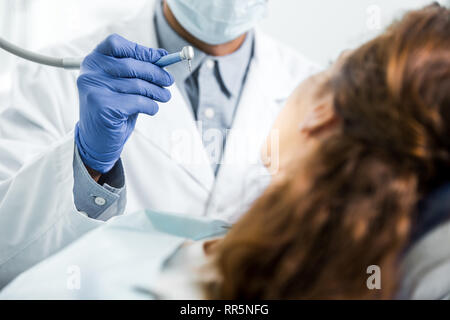 7/8-Ansicht von Zahnarzt in weißen Mantel Holding dental Instrument in der Nähe der Patientin Stockfoto