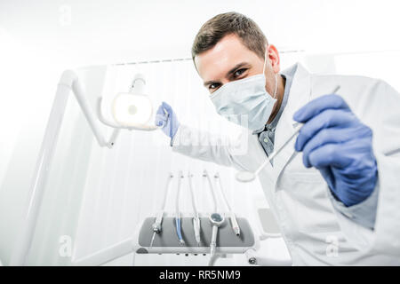 Zahnarzt in Latex Handschuhe und Maske Holding zahnmedizinische Lampe und zahnmedizinische Instrument in den Händen Stockfoto