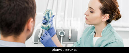 Selektiver Fokus der weiblichen Zahnarzt holding Zähne Modell und Zahnbürste in der Nähe von Patienten Stockfoto