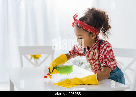 Cute afrikanische amerikanische Kind in gelbe Gummihandschuhe Waschtisch mit Reinigungsspray und rag Stockfoto