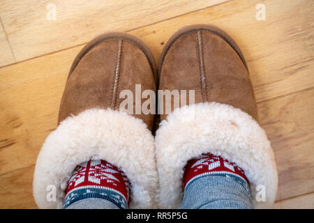 Gemütliche sherpa Leder slipperes Haus mit warmen Socken. Füße in Hausschuhen auf Holz. Raum für Raum kopieren Stockfoto
