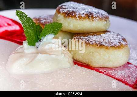 Traditionelle russische Süße gebratener Käse Kuchen elegant auf einem Teller mit saurer Sahne und Marmelade, mit Zucker bestreut in Russland Stockfoto
