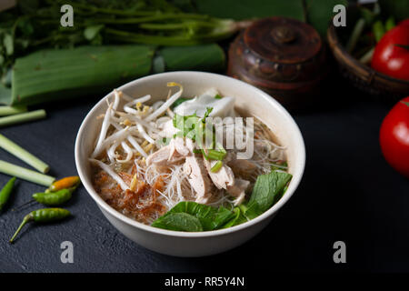 Asiatische Reisnudeln Suppe und Hühnchen in der Schüssel auf dunklem Hintergrund. Stockfoto