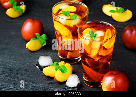 Pfirsich Eistee in ein Glas mit Minze auf einer schwarzen Holztisch (selektive Fokus). Stockfoto
