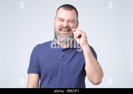 Lächelnd attraktiver reifer Mann mit Bart in blauen T-Shirt direkt in die Kamera schaut Stockfoto