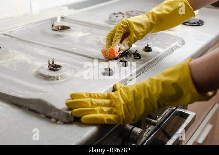 Die Hände der Frau in gelb Handschuhe Reinigung Gasherd in der Küche. Waschmittel und Seife Schaum auf Gas Herd Oberfläche. Stockfoto