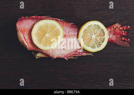 Zwei saftige Zitronen Scheiben liegen auf frischen roten Fischen. Der Fisch wird aufgerufen, Seebarsch. Sie mariniert und wird bald sehr lecker verurteilt werden. Stockfoto