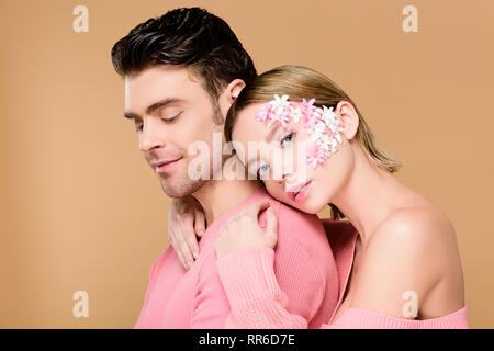 Schöne Frau mit Blumen auf dem Gesicht umarmen Mann isoliert auf beige Stockfoto
