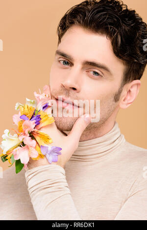 Stattlicher Mann mit alstroemeria Blumen an Hand berühren Gesicht isoliert auf beige Stockfoto