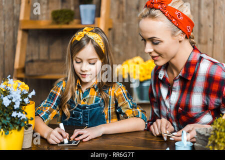 Fröhliches Kind schreiben mit Kreide auf kleine Schiefertafel in der Nähe von Mutter Stockfoto