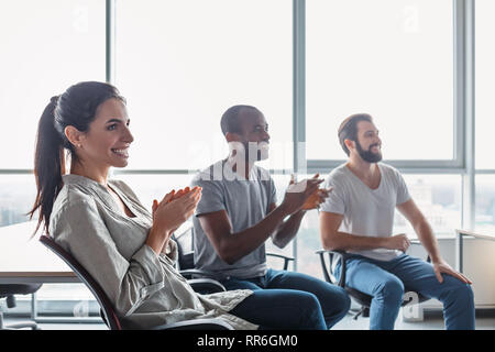 Gruppe von attraktiven multirassischen Lachen Geschäftsleute reden und scherzen Sitzen auf Stühlen in hellen modernen Büro , multi-ethnischen Business te Stockfoto