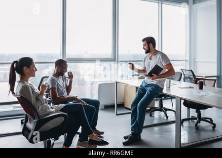 Gruppe von attraktiven multirassischen Lachen Geschäftsleute reden und scherzen Sitzen auf Stühlen in hellen modernen Büro , multi-ethnischen Business te Stockfoto