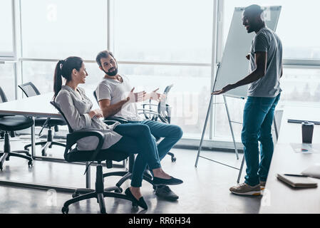 Gruppe von attraktiven multirassischen Lachen Geschäftsleute reden und scherzen Sitzen auf Stühlen in hellen modernen Büro , multi-ethnischen Business Team Spaß haben, Diskussion von Fragen in der Sitzung Stockfoto