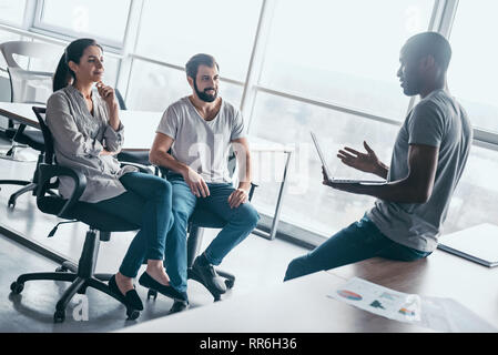 Gruppe von attraktiven multirassischen Lachen Geschäftsleute reden und scherzen Sitzen auf Stühlen in hellen modernen Büro , multi-ethnischen Business Team Spaß haben, Diskussion von Fragen in der Sitzung Stockfoto