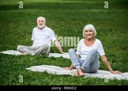 Gerne älteres Paar sitzen in Entspannung stellt sich auf Yoga Matten auf grünen Rasen Stockfoto
