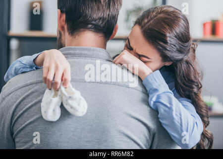 Frau weinen, umarmte man und Holding Baby Socken zu Hause, trauernde Unordnung Konzept Stockfoto