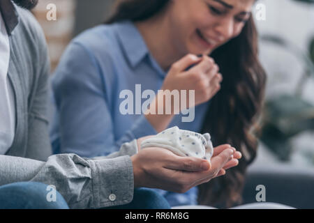 7/8-Ansicht der Mann hält Baby Socken, während die Frau zu Hause weinen, trauern Unordnung Konzept Stockfoto