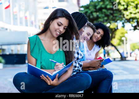 Happy learning lateinamerikanischen Studentin mit internationalen Gruppe von Studenten Outdoor im Sommer in der Stadt Stockfoto