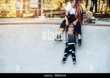 Schöne junge Hipster Mama hält ihren kleinen Sohn durch die Hände Stockfoto