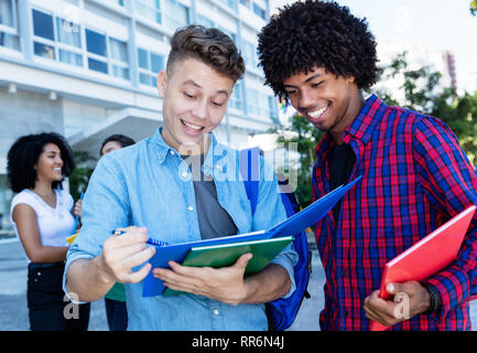 Kaukasische männliche Kursteilnehmer lernen mit afrikanischen amerikanischen Freunden im Freien im Sommer in der Stadt Stockfoto