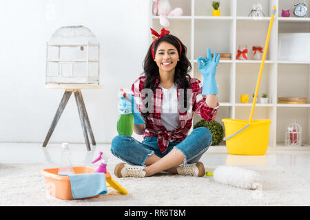 Lächelnd afrikanische amerikanische Frau in Blau Gummi Handschuhe sitzen im Lotussitz und zeigen ok Zeichen Stockfoto