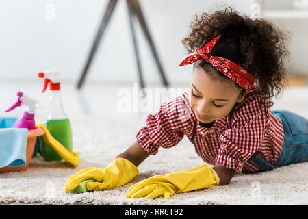 Cute afrikanische amerikanische Kind Reinigung Teppich in gelbe Gummihandschuhe Stockfoto