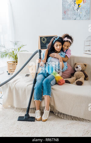 Adorable african american Kind umarmen müde Mutter sitzt auf einem Sofa Stockfoto