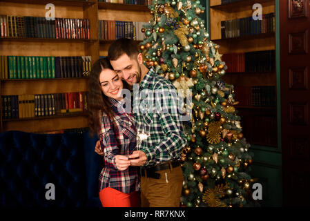 Junge schöne Küsser und brennenden Wunderkerzen. Liebende Paar in Weihnachten eingerichtete Zimmer. Stockfoto