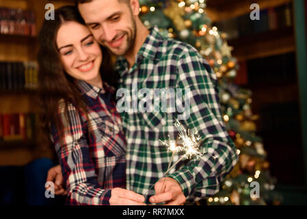 Wunderkerzen und ein Kuss für Weihnachten. Junge schöne Küsser und brennenden Wunderkerzen. Liebende Paar in Weihnachten eingerichtete Zimmer. Stockfoto