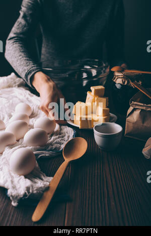 Junge Frau Kochen Kuchen auf braun Küchentisch. Nahaufnahme der Hand des Weiblichen die gewürfelte Butter, Eier und Mehl zu Teig für Kreis vorbereiten. Stockfoto