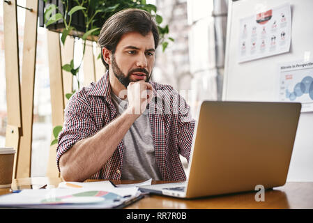 Ernster Mann in Freizeitkleidung über neue Business Plan denken, sitzen mit Laptop. Nachdenklicher Mann kümmert sich um die erfolgreiche Zukunft. Nachdenklicher Kerl zum Testen neuer Software Stockfoto