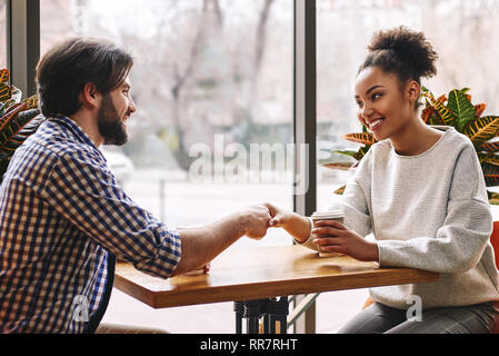 Seitenansicht Porträt von zwei erfolgreiche Geschäft Leute, Mann und Frau, lächelnd und schütteln Hände über Tabelle während der Sitzung im Cafe. Afrikanische amerikanische Frau und kaukasische dunkelhaarigen Mann Stockfoto