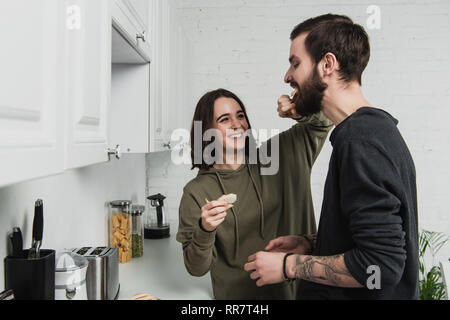 Schöne lächelnde Frau Fütterung stattlicher Mann mit Toast beim Frühstück in der Küche Stockfoto