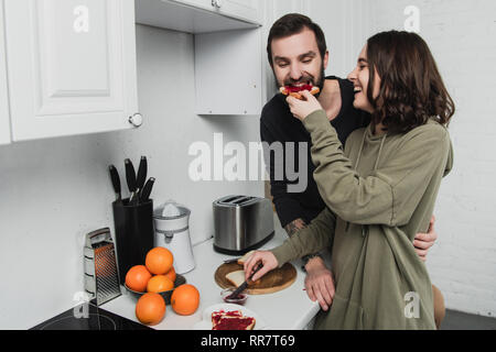 Lächelnde Frau füttern Mann mit Toast beim Frühstück in der Küche Stockfoto