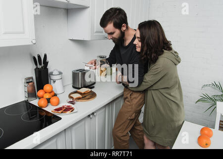 Schöne junge Paar unter Foto von Toast auf dem Smartphone beim Frühstück in der Küche Stockfoto