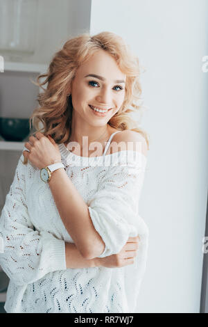 Lächelnd curly Frau in Weiß Strickpullover an Kamera suchen Stockfoto