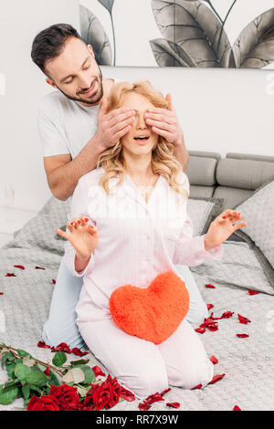 Mann sitzt auf dem Bett mit Rosen und für die Freundin Augen Stockfoto